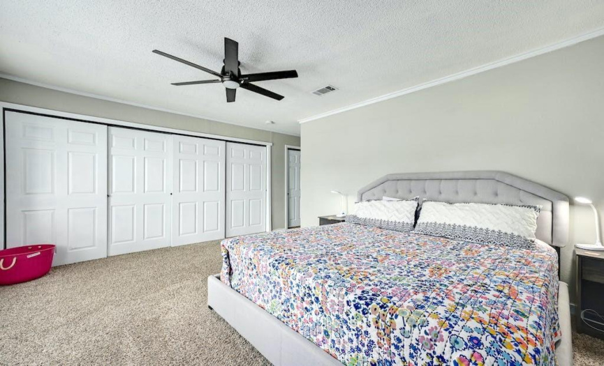 The primary bedroom suite features crown molding, expansive sliding door closets, carpet, and large, paned windows overlooking the front yard. 