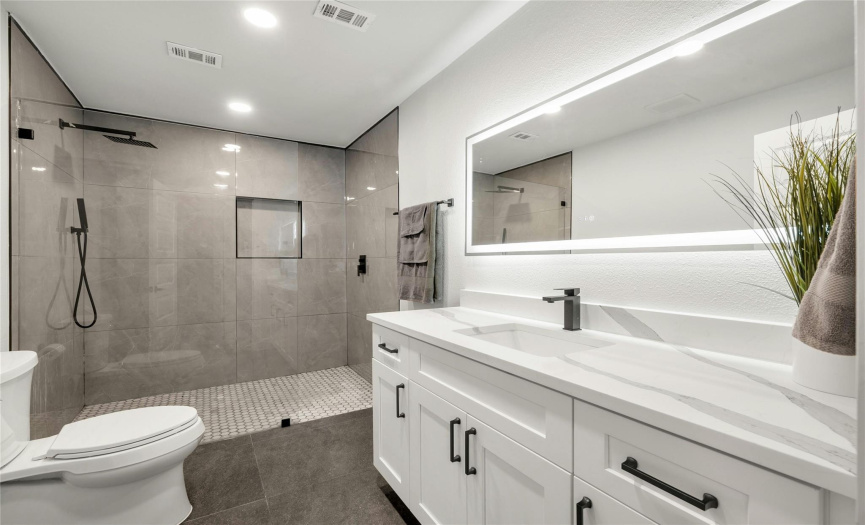 The spacious additional bathroom is located close to the additional bedrooms. It offers a large double vanity with a stunning quartz countertop, updated cabinetry, a large frameless LED mirror, an over-sized walk-in shower with a modern tile surround, a large custom niche, and black fixtures.