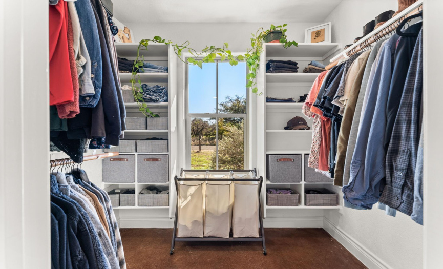 Spacious walk in primary closet has a large window for natural lighting and the ability to get some fresh air as well as custom shelving units.