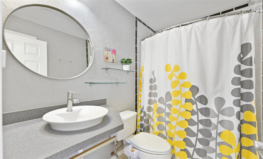 Primary bathroom with stylish bowl sink, low profile glass shelving, and a tub/shower combo.  