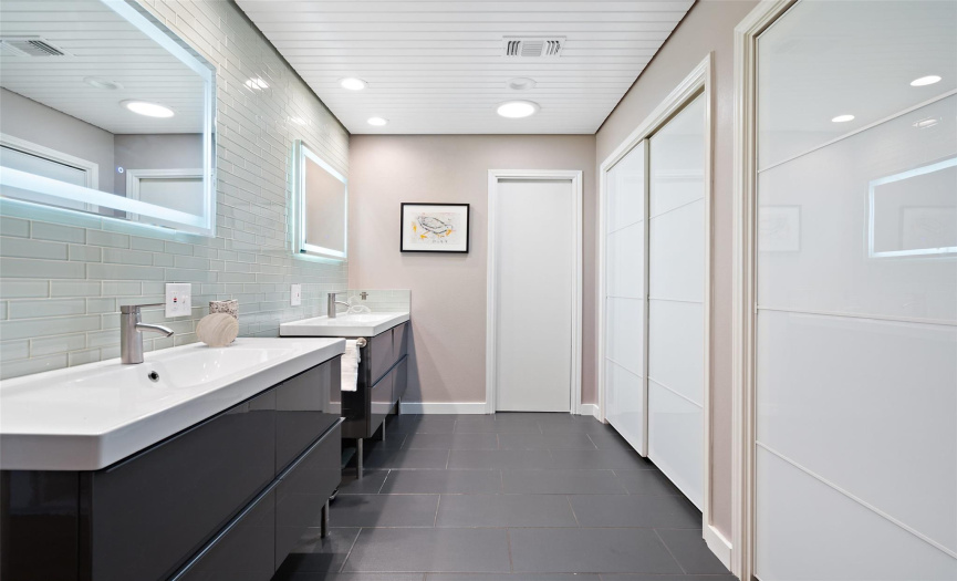 Spacious ensuite bathroom featuring double vanities, a tiled accent wall, LED light-up mirrors, and ample closet space
