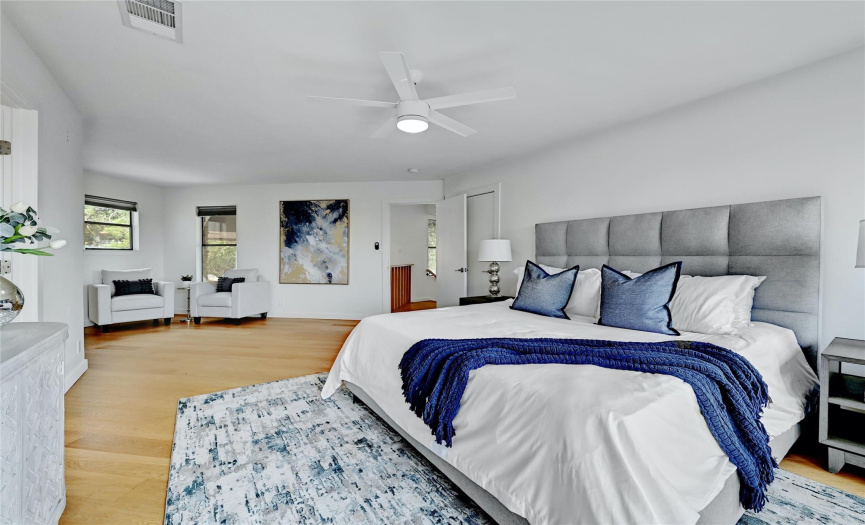 The primary bedroom features wood flooring, a ceiling fan, a sitting area, and direct access to a private balcony.