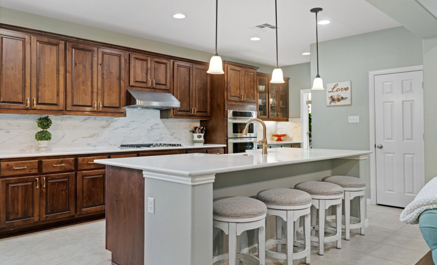 Adorned with ample cabinetry, the kitchen boasts built-in stainless-steel appliances, marble-style backsplash, and opulent quartz countertops. (Butler pantry on the right side of ovens & refrigerator sits across from butler pantry), which leads into the dining room. 