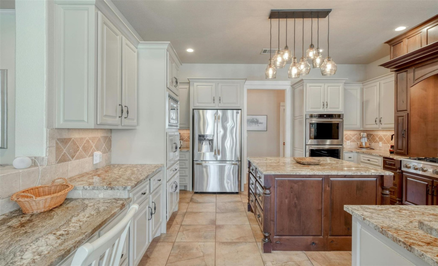 Stunning white kitchen with granite countertops, bar seating, & top-of-the-line stainless steel appliances including a 6-burner gas stove with a pot filler & double oven. 