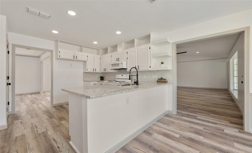 The kitchen is beautifully updated with elegant white cabinets, modern cabinet pulls, LED recessed lighting, gray tone back splash, and gleaming granite all go great together!
