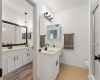 The additional bathroom has large separate vanity areas with sinks, modern light fixture, a make-up sitting area, white cabinets, black faucets, a medicine cabinet, cabinet pulls, and a nice sized tub/shower combo.