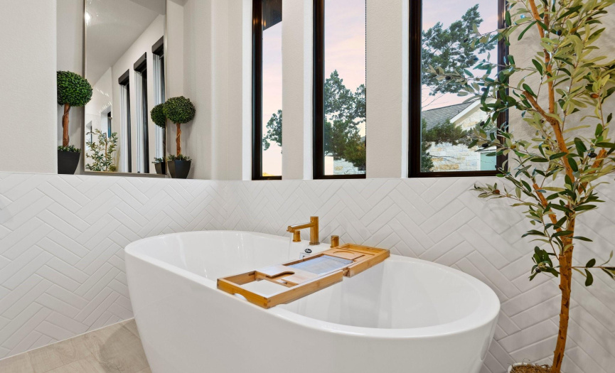 The freestanding soaker tub is nestled amidst a backdrop of herringbone pattern tile. Abundant natural light floods the space, creating a serene and inviting atmosphere for relaxation and rejuvenation.
