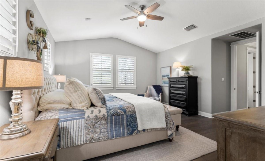 Spacious primary bedroom with a vaulted ceiling, wood floors & plantation shutters.  