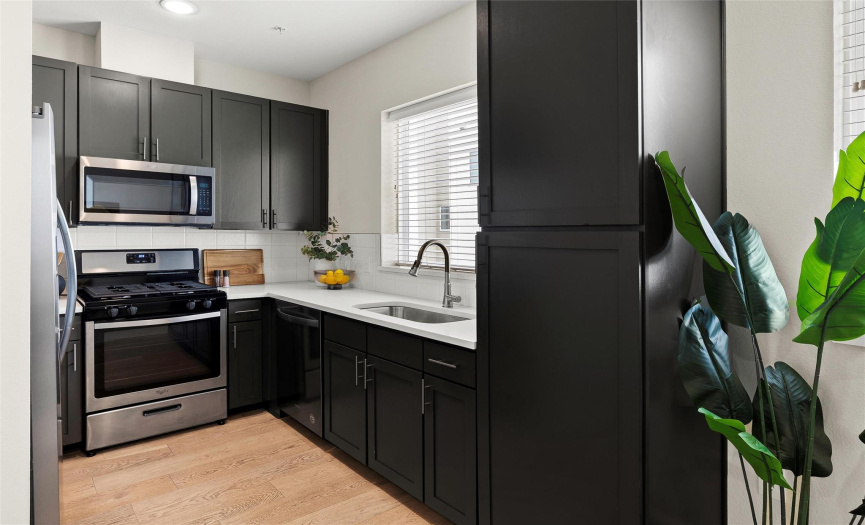 The modern kitchen features gray shaker-style cabinetry, trendy quartz countertops, a tile backsplash, and sleek stainless-steel appliances including a gas range.