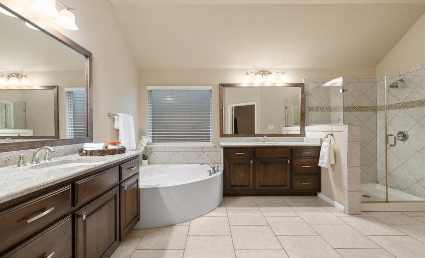 This spa-like ensuite bathroom provides a relaxing garden tub, frameless glass-enclosed walk-in shower with tile surround, large walk-in closet, linen closet, and a private commode. 