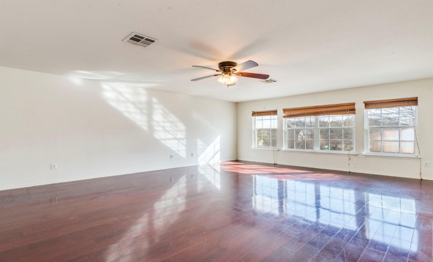 Expansive primary bedroom with gleaming hardwood floors, ceiling fan, and large windows creating a bright and airy retreat.
