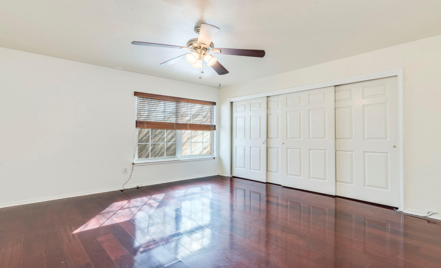 Inviting bedroom featuring rich  faux hardwood floors, ceiling fan, and ample closet space, offering comfort and practicality.