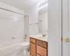 Compact and clean secondary bathroom with a full tub, bright lighting, and warm wood cabinetry; ideal for guests and family use.