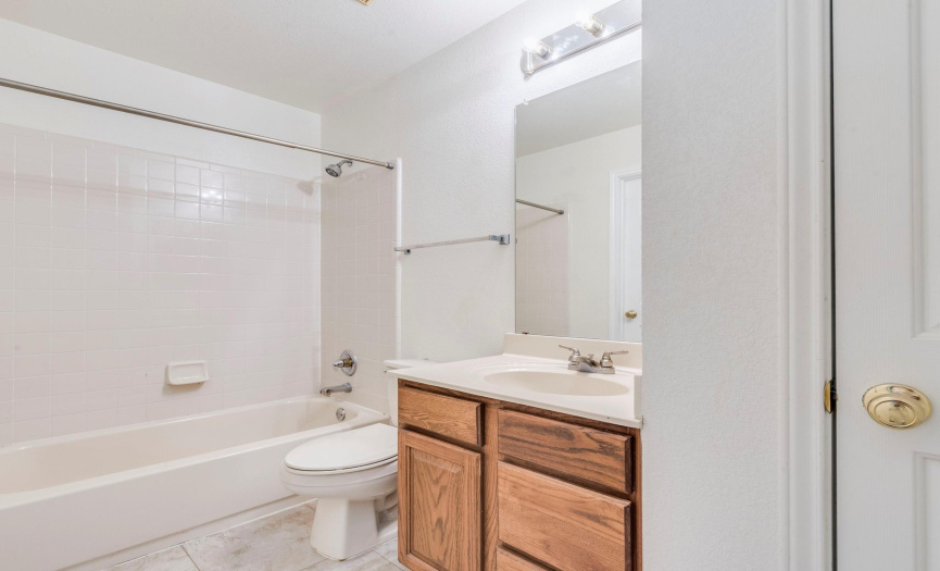 Compact and clean secondary bathroom with a full tub, bright lighting, and warm wood cabinetry; ideal for guests and family use.