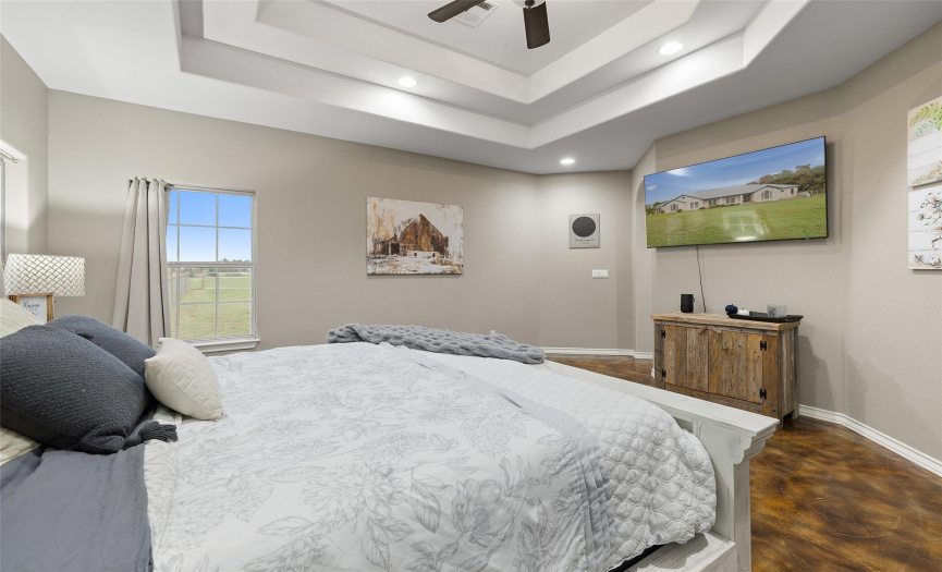 The main bedroom portion of this deluxe primary suite features elegant tiered tray ceilings, peaceful views, and plenty of space for a king sized bed, furniture, and a seating area. 