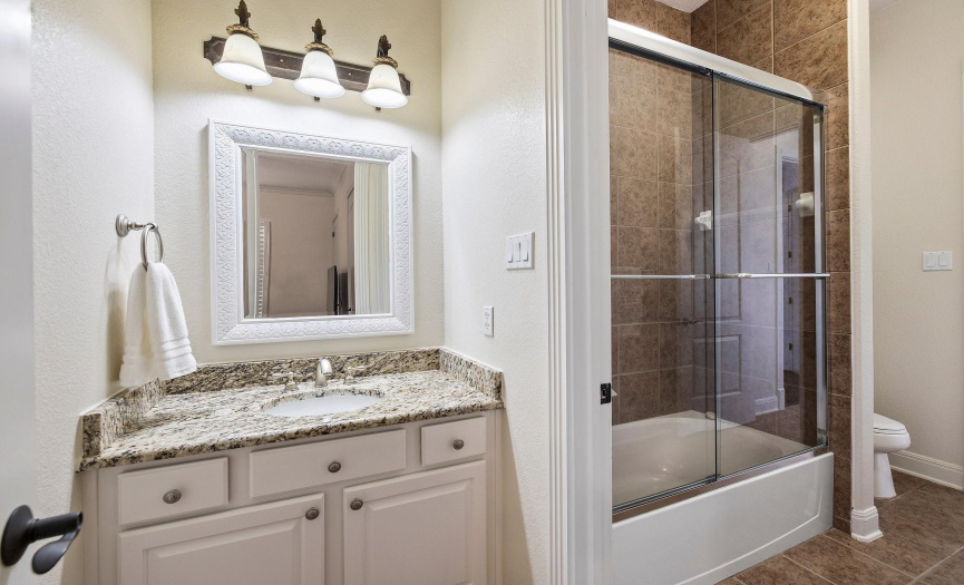 Neat secondary bathroom with granite counter and glass-enclosed shower