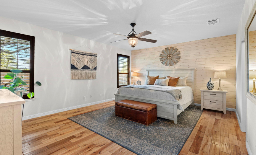 The primary bedroom is a peaceful retreat with a whitewashed focal wall, hardwood floors and private views of the backyard. 