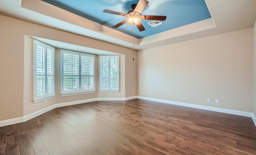 Primary bedroom downstairs has a tray ceiling. Plantation shutters grace the bay windows.