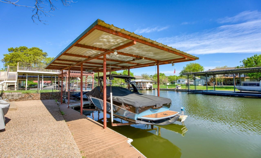 Beyond the porch, a manicured lawn leads to the dock, complete with a covered boat slip with lift, 2 jet ski ramps, and a storage shed, providing easy access to the water for boating, swimming, and other recreational activities.