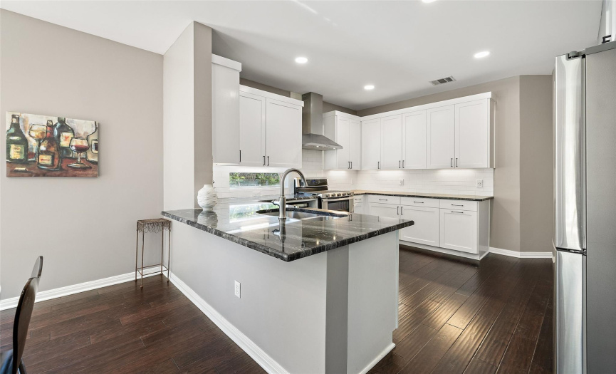 The bright kitchen boasts a bar, granite countertops, and recessed lighting.