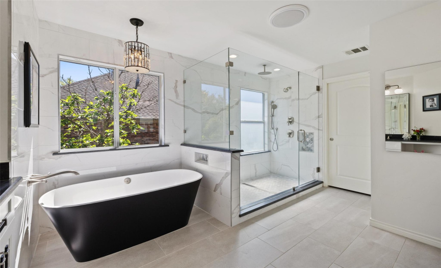 The primary bathroom features a free-standing high end soaking tub with a stylish overhead light fixture, tile flooring, and a grandiose walk-in shower with a rain showerhead.