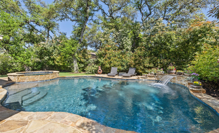 A thoughtfully designed pool with a waterfall surrounded by tall trees and excellent landscaping.
