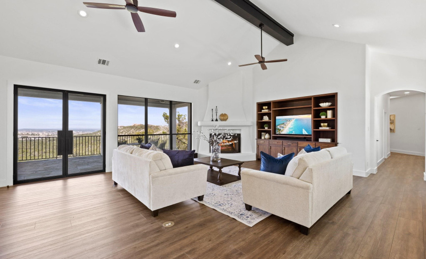 Bright, airy living space with high ceilings, adobe fire place and wall-to-wall windows offering stunning views, perfect for elegant yet comfortable living.
