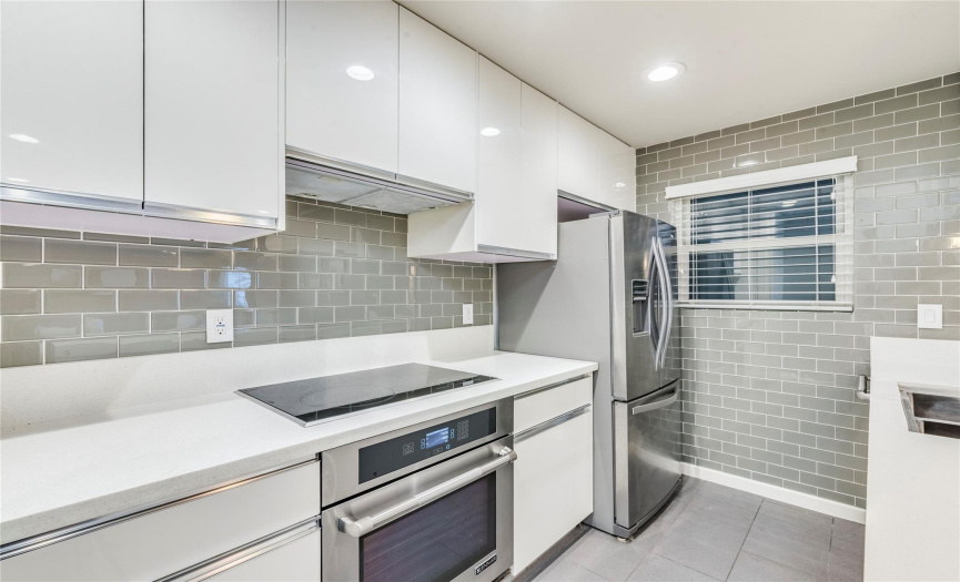 Sleek modern cabinetry, quartz countertops, glass wall tile backsplash, stainless steel appliances