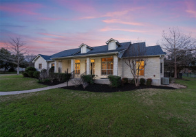 Welcome to a serene Texas twilight, where this stunning stone-clad residence awaits. The gentle glow from the windows promises a warm welcome, accentuating the charming facade. The elegant landscaping frames a walkway leading to an inviting front porch, setting the stage for cozy evenings under the vast Texas sky.