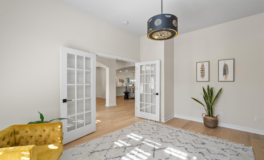 Step into sophistication with this bright foyer, where French doors open to a spacious, light-filled living area. The modern chandelier adds a touch of elegance, while the rich hardwood floors lead you seamlessly through the home's open layout, offering a preview of the refined lifestyle that awaits.