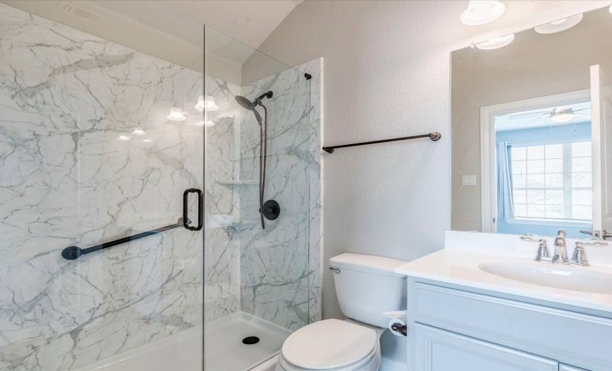 The guest ensuite bath features a gorgeous frameless glass enclosed walk-in shower with stylish tile backsplash and a safety handrail. 