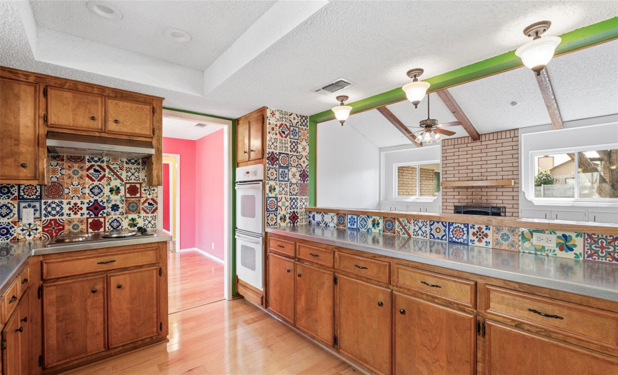 The colorful kitchen is lined with decorative tile backsplash and features built-in double ovens and an electric cooktop. 