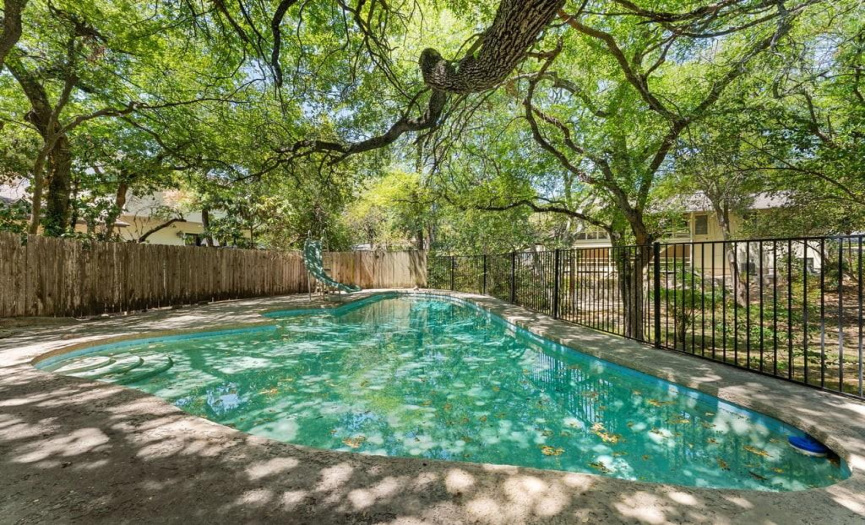 A bridge over the creek leads to a stunning pool area, providing an inviting space for warm-weather gatherings