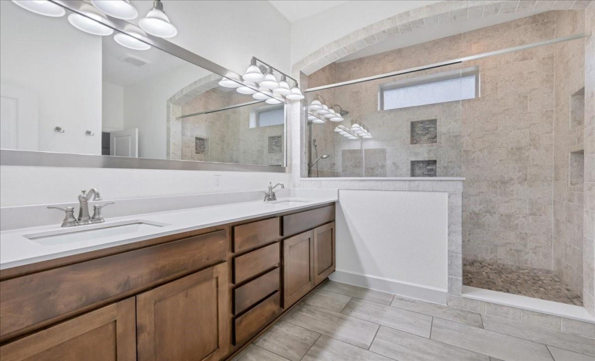 The primary bathroom has a large double vanity with quartz countertops and a custom super shower.