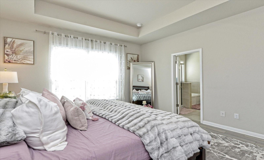 Spacious primary bedroom has added drama with the coffered ceiling and huge picture window offering natural light, overlooking the green space and pond.