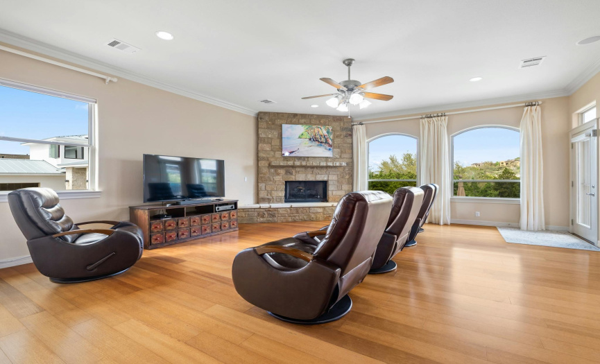 The heart of the home lies in the spacious living room, featuring a cozy corner stone fireplace, built-in speakers, and windows that overlook the entertainer's dream backyard oasis