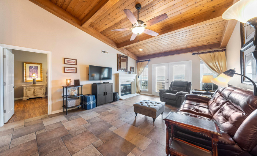 Step into the living area adorned with distinctive cedar and beamed vaulted ceilings, complemented by elegant tile flooring and a bespoke wood-burning fireplace with a custom surround.