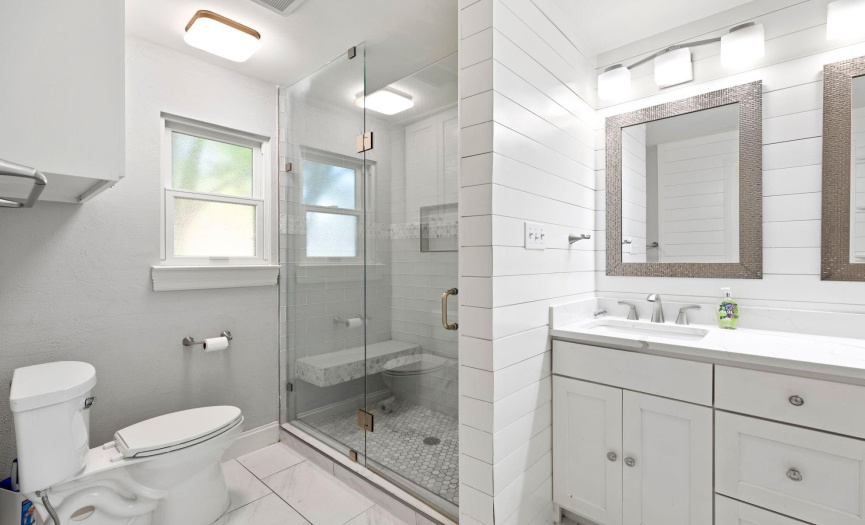 The walk-in shower is a standout, adorned with subway tile, complimenting mosaic floor tile and a convenient bench for seating. This setup is complemented by sleek, frameless glass that adds a touch of modern sophistication.