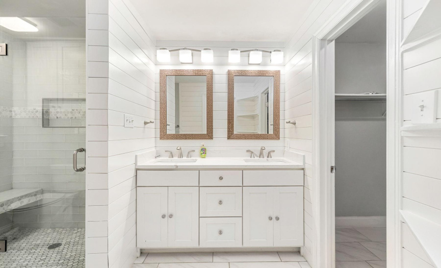 The primary bathroom exudes a bright and elegant charm, decorated with pristine light shiplap that enhances its airy feel. It features dual vanities that provide ample space for morning and evening routines. 