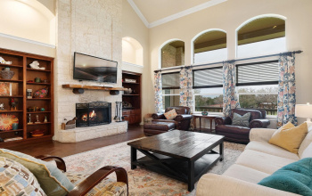 The jaw-dropping living room steals the show with its vaulted ceilings, floor-to-ceiling stone fireplace, built-in bookshelves, and a wall of windows that showcase breathtaking hill country views and incredible sunsets