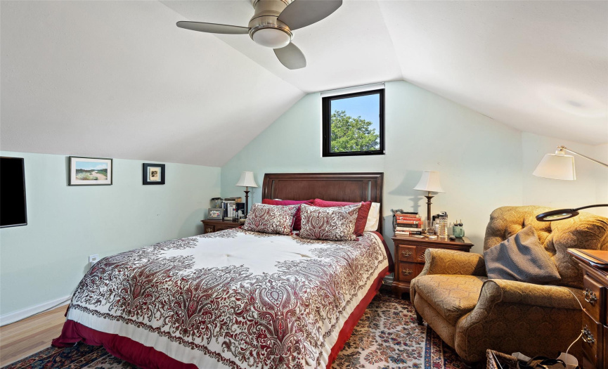 High cathedral ceilings, wood flooring, and a ceiling fan in this bedroom.