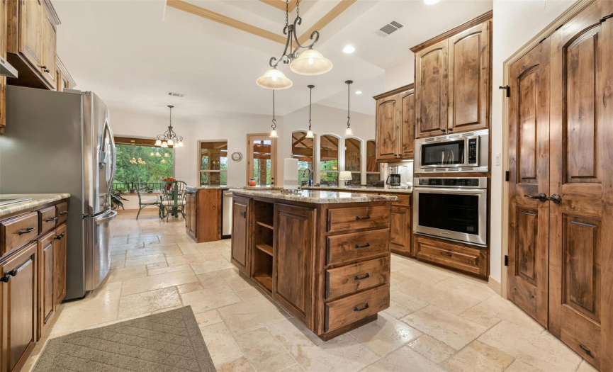 The cooktop is to the left of the refrigerator. The dishwasher is a Bosch. The kitchen also features a coffered ceiling and recessed lighting. The walk-in pantry has double doors.