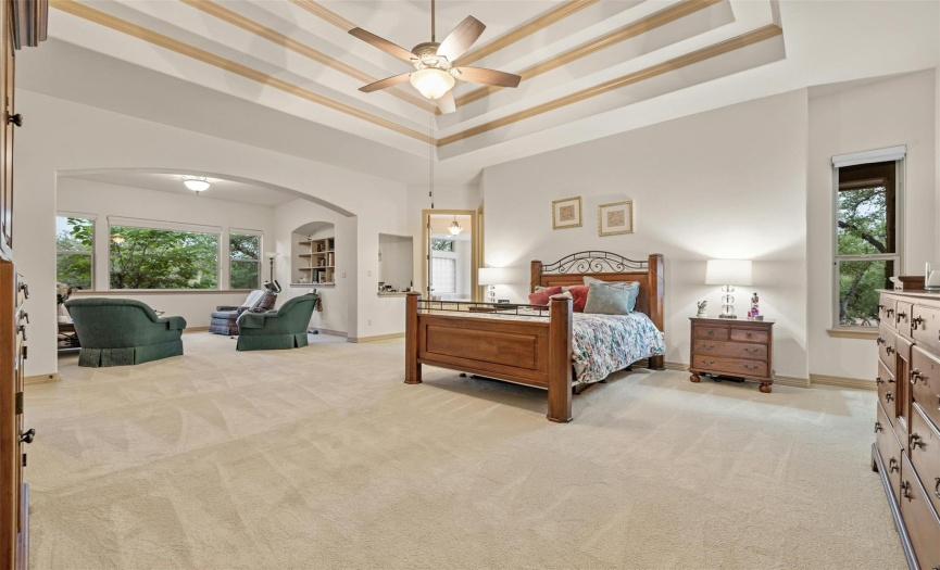 This sophisticated master suite features a coffered ceiling and large sitting area with built in shelving and a TV on the opposite wall. 