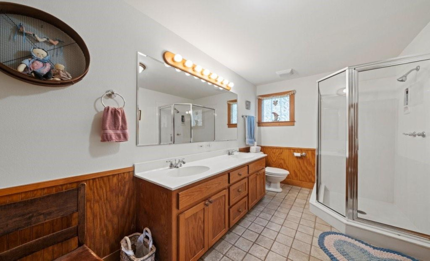 The en suite bath for the primary offers two sinks, bead board wainscoting and easy care tile flooring.