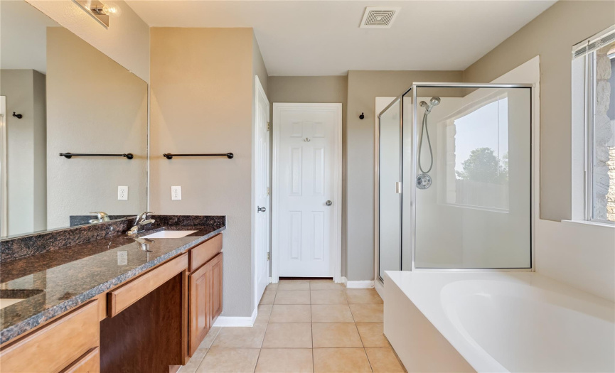 Unwind in the luxurious en-suite bath, featuring a granite-topped dual vanity, soaking tub, and separate walk-in shower.