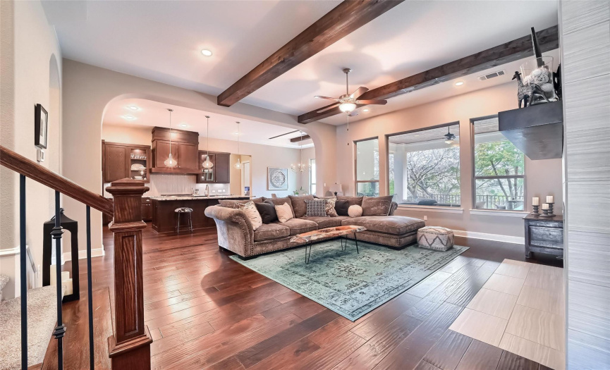 Luscious wood floors & natural wood beam ceiling = spectacular living room! Note the large fixed glass window which over-looks the covered patio and the woodsy views.