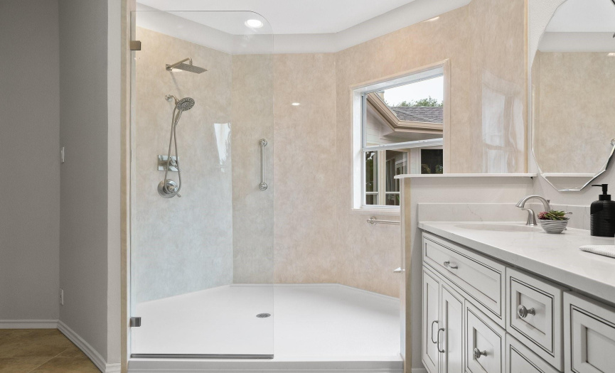 Wash away your worries in the oversized walk-in shower with frameless glass doors, overhead rain shower, bench seating, and safety rails. 