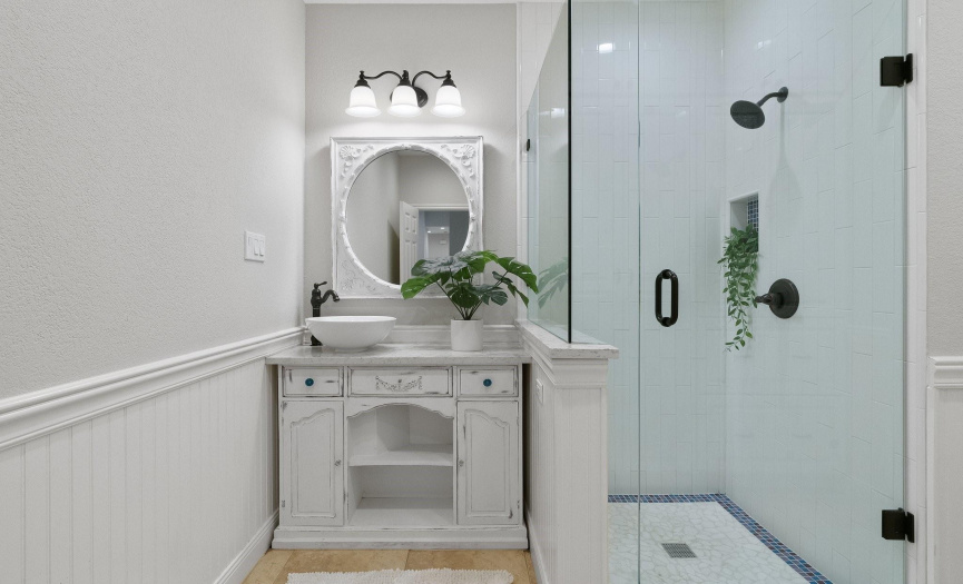 The full guest bathroom is beautifully updated with a spa-like frameless glass enclosed walk-in shower and a lovely French vintage inspired vanity, gorgeous finishes, and wainscoting along the wall. 