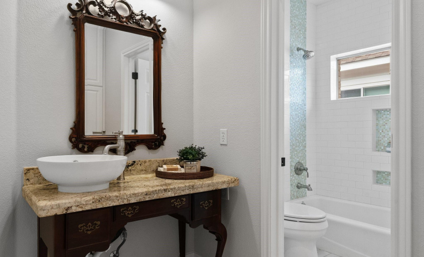The full secondary bathroom features a credenza-style vanity with a granite countertop and a raised bowl sink. The separate water closet hosts the shower/tub combo & commode.