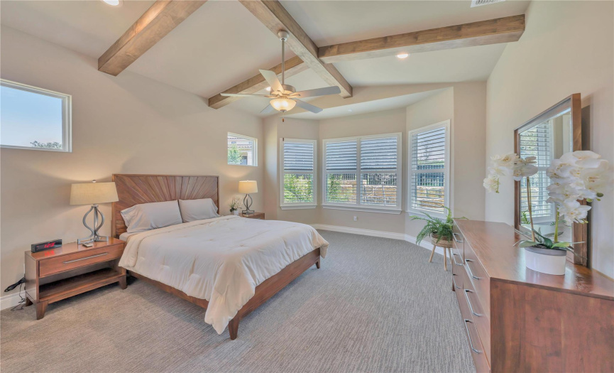 The primary suite is at the rear of the home to ensure privacy. The bay window offers a sitting area. Ceiling beams are an upgrade. Custom shutters filter the light in this large room.